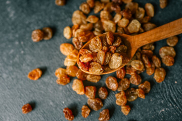 Raisins in a wooden spoon scattered on a black background