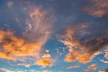 Morgen- oder Abendhimmel mit aufgelockerter, vom Wind verwirbelter, orangefarbener Bewölkung, bei klarer Luft und blauem Himmel