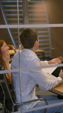 Man in VR headset looking at objects in virtual reality with colleagues. People sitting in armchairs at the desk and interacting with 3d visualization. Mix raced. Slow motion. Vertical shot.