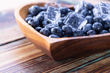 Fresh blueberries with ice cubes close-up on a wooden plate