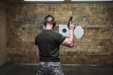 An athletic man with a pistol in his hand is training at a shooting range.