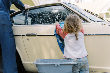 toddler girl and her father washing car in driveway together