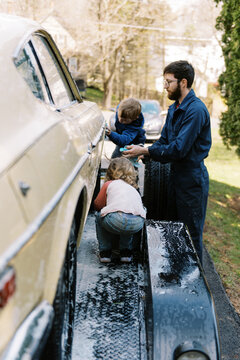 father washing old classic car on trailer with his kids outdoors