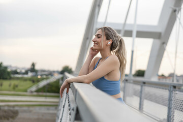 Obraz premium Smiling woman listening music after training on the brigde