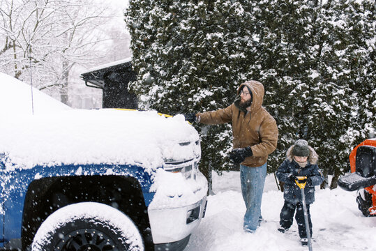 father and son clearing snow off truck and driveway together