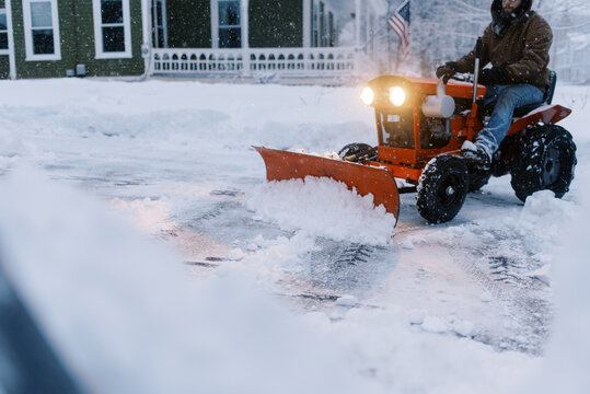man using old tractor to snow plow his driveway at dusk