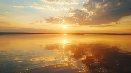 Obraz premium Breathtaking sunset over serene lake with golden sky and clouds reflecting on calm water. Perfect for nature and landscape themes.