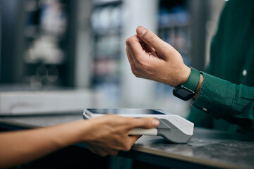 A male with a smartwatch pays his bill over it, holding it close to the payment machine at the...