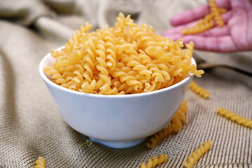Fusilli pasta in a white bow with a blurred hand at the back. Close-up fusilli texture in a bow....