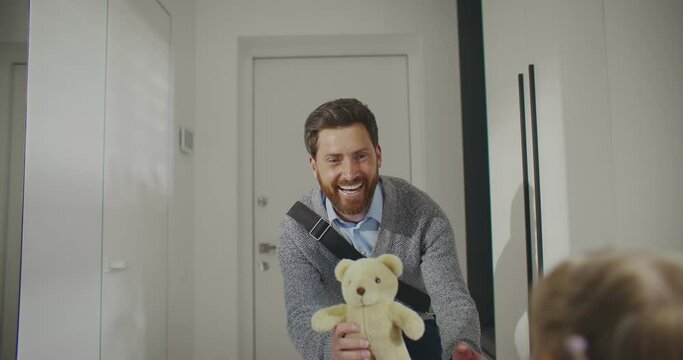 Close view of Caucasian man with beard closing door behind him. Male entering apartment with toy for beloved daughter with blonde hair. Coming home after hard working day. Showing love to family.