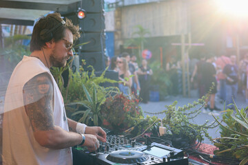 Tattooed DJ playing for dancing people on the dancefloor outdoors