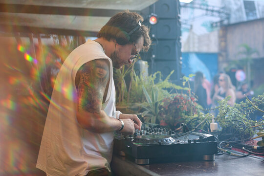 Tattooed DJ wearing sunglasses and headphones playing at party