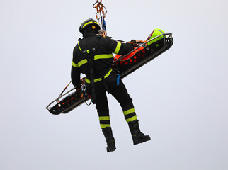 firefighter with stretcher and injured person hanging in the air attached to rope during rescue