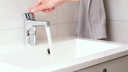 Human's hand opens and closes a water faucet, strong water pressure, tap with clean running water in the modern white bathroom. Fresh drinking water loss and saving concept video - Powered by Adobe