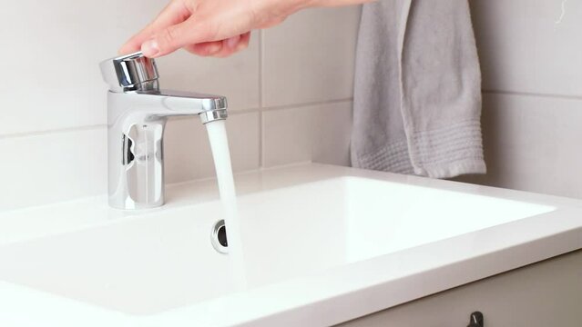 Human's hand opens and closes a water faucet, strong water pressure, tap with clean running water in the modern white bathroom. Fresh drinking water loss and saving concept video