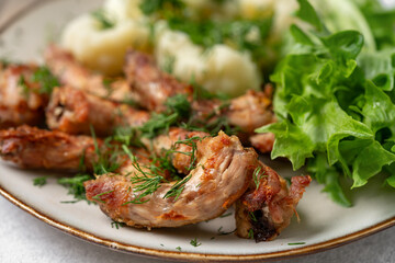 Baked or fried chicken necks in barbecue sauce, cauliflower and lettuce leaves on a plate on the...
