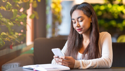 A young black girl is seated at a table, engrossed in looking at her phone. She appears focused on...