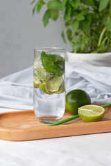 Mojito cocktail drink in glass, lime, drinking straw, mint in pot on white marble table background