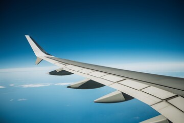 Fototapeta premium Airplane wing against blue sky, flaps extended, pointy tip, horizon in background