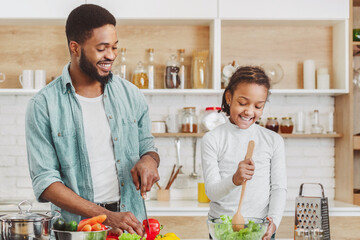 Cute little african girl helping her dad to make salad, cooking together, kitchen interior, copy...