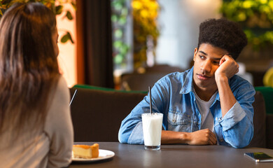 Two African American teenagers are seated at a cafe table. One appears deep in thought while the...