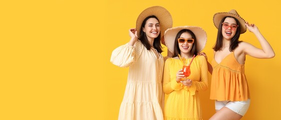 Beautiful young women in beach hats and with glass of cocktail on yellow background with space for...