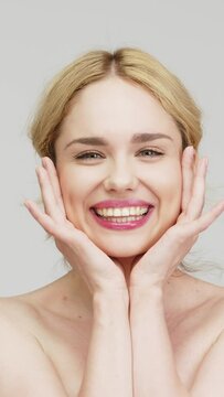 Vertical video. Close-up of a happy blonde girl showing a snow-white, beautiful smile against a light background. Concept of dental services and dental care products.