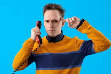 Displeased young man with phone receiver twisting finger near temple on blue background