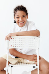 Young boy sitting stylishly on white chair with hands gracefully resting on the back