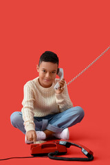 Little African-American boy with two telephones on red background