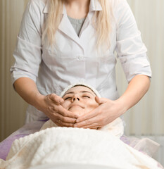 Obraz premium Young woman enjoying facial massage, lying on spa bed indoor at beauty salon.