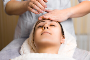 Young woman enjoying facial massage, lying on spa bed indoor at beauty salon.