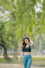 Asian woman trainer is engaged in fitness in public park. Sporty woman does exercises in the open air. Healthy lifestyle, sports outdoor activities in park