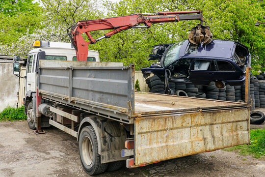 A hydraulic loader loads a abandoned car wreck onto a truck to take it to a recycling site