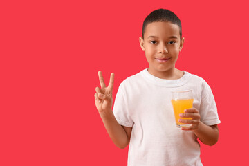 Little African-American boy with glass of orange juice showing victory gesture on red background