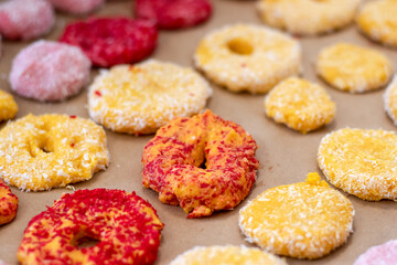Close-up of yellow and red cookies, ready to bake, in coconut flakes on a baking sheet.