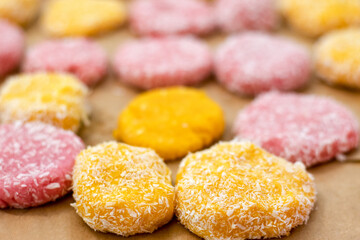 Close-up of yellow and pink raw cookies, ready to bake, in coconut flakes on a baking sheet.