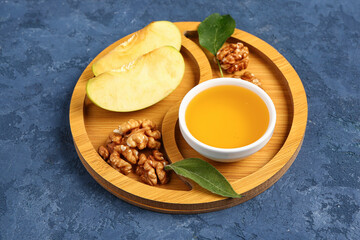 Wooden board with bowl of sweet honey, walnut and apple on blue background