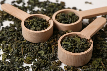 Wooden spoons with dry green tea leaves as background, closeup
