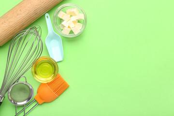 Bowls with butter, oil and kitchen utensils for preparing bakery on green background