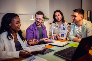 A group of four young people from diverse backgrounds gather around a model wind turbine. They share their thoughts and ideas about sustainable energy sources. 