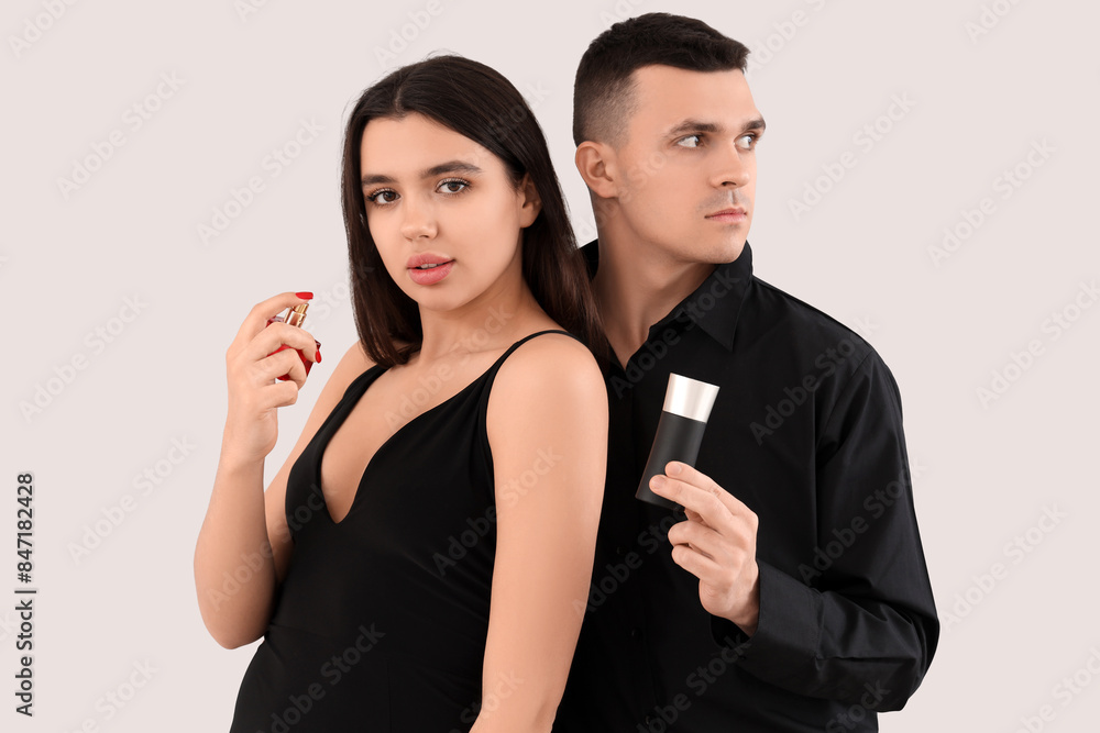 Poster Elegant young couple with bottles of perfume on light background