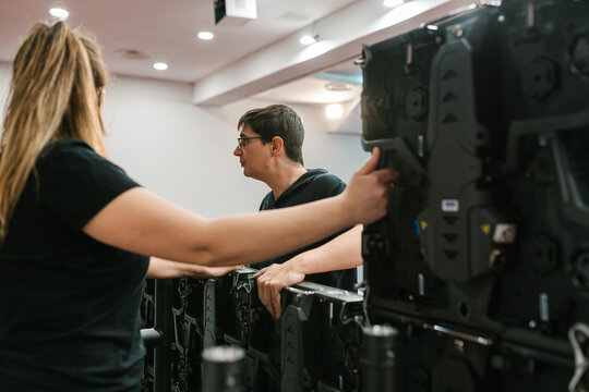 Professional technicians standing with LED display in auditorium