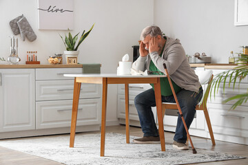 Portrait of sad senior man with tissues sitting at table in kitchen