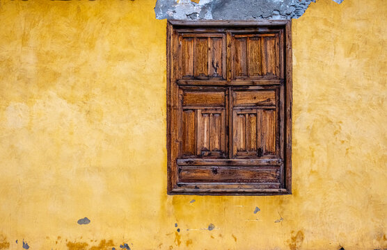 Colorful, old distressed wooden window and yellow plaster wall