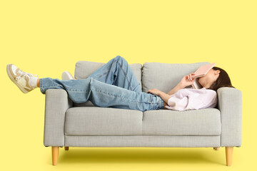 Obraz premium Beautiful young woman with book sleeping on sofa against yellow background