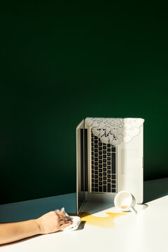 Hand wiping spilled coffee on table with a laptop