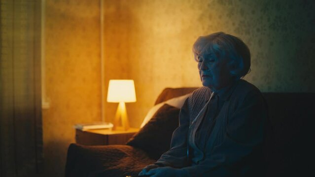 Lonely elderly woman wearing nasal cannula watches TV on sofa, solitude