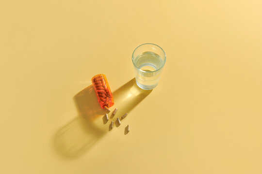 Bottle of pills capsule and glass with pure water on yellow