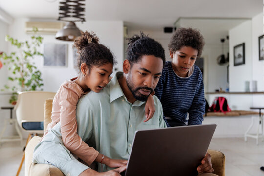 Children looking at father working on laptop
